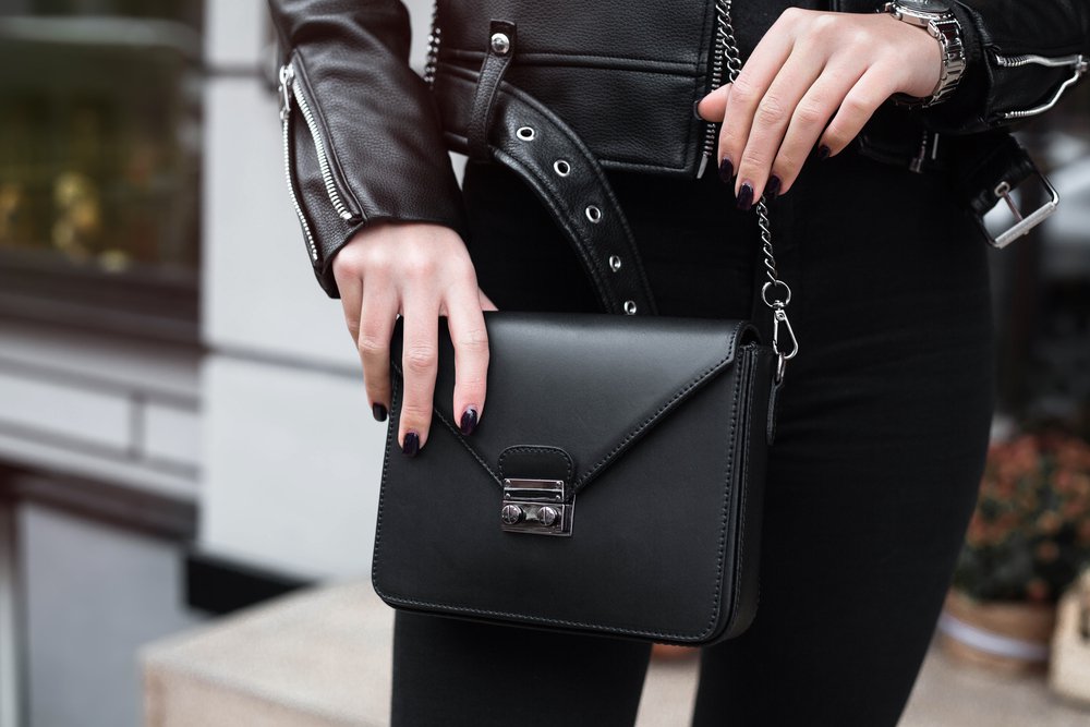 Young stylish beautiful woman walking in street, wearing pink trendy leather jacket, holding purse, black shirt, fashion outfit, autumn trend, spring fashion,accessories, hands close-up,copy space.